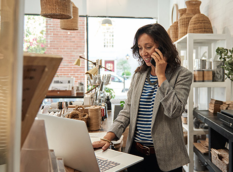 An owner of a modern retail outlet shop is on the phone while browsing on her laptop.