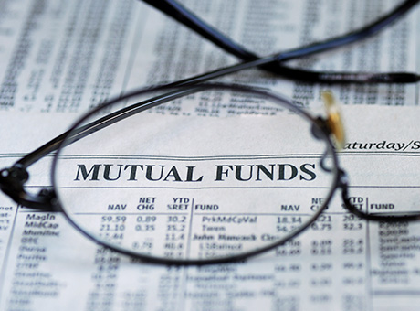 Newspaper with text 'Mutual funds' closely through a pair of glasses.