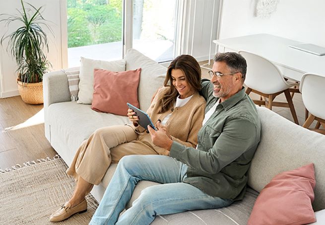 Man and women smiling on couch looking at tablet