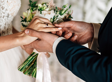 A couple holds hand on their wedding day as they exchange wedding rings.