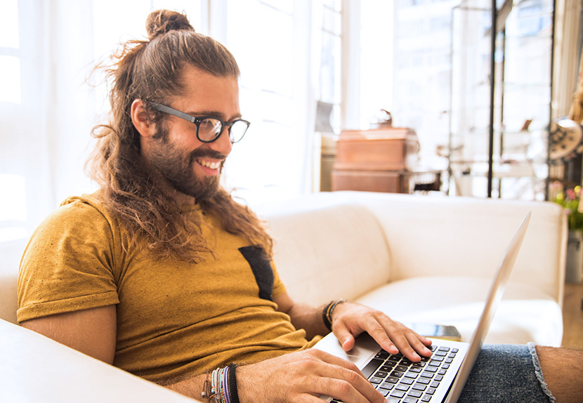 Man smiling while working at his computer, sitting on couch