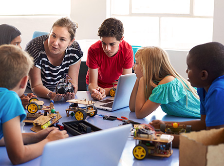 A grown-up is instructing a children's group in robotics at a table.
