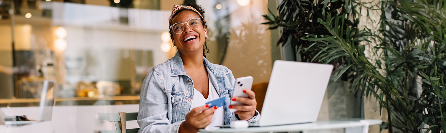 Person sitting at a computer, holding a phone and credit card, while they work on their savings goals.
