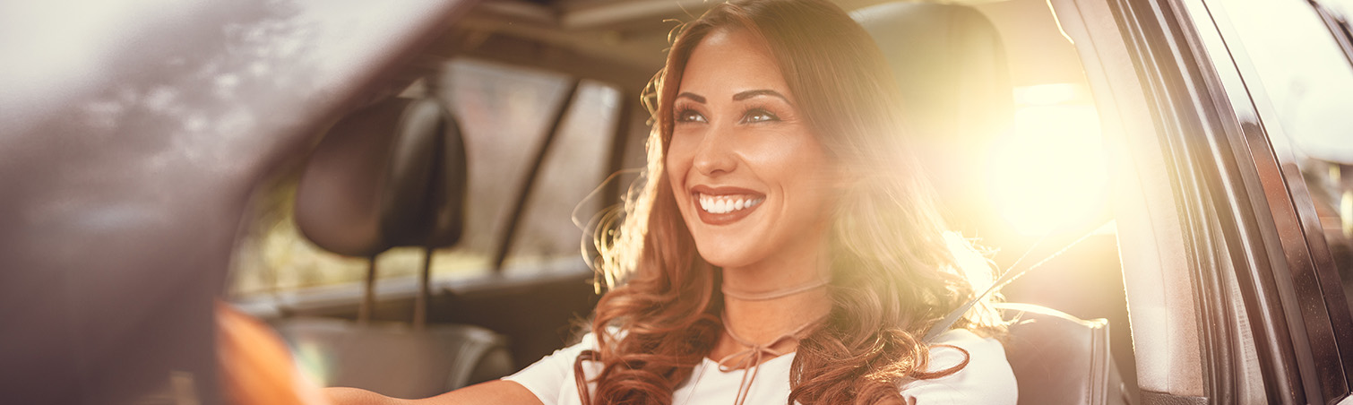 A smiling member is seen driving their car during the day.