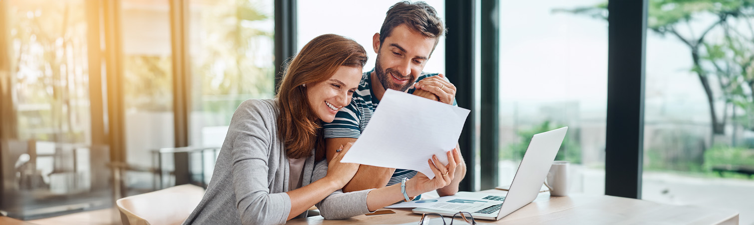 An excited couple sits at their dining room table as they read tips on saving up for their wedding day. 