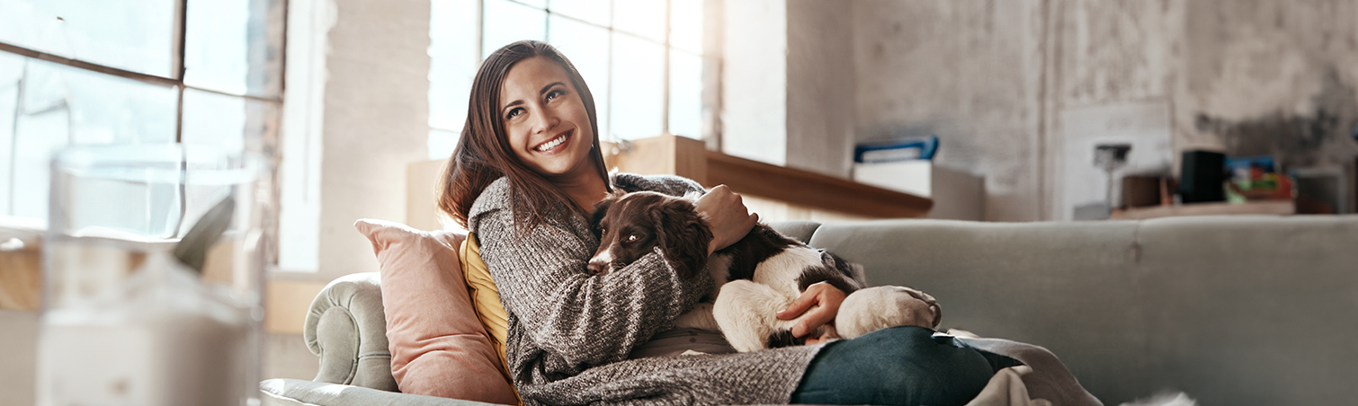 A first-time homebuyer smiles while sitting on the couch with her dog.