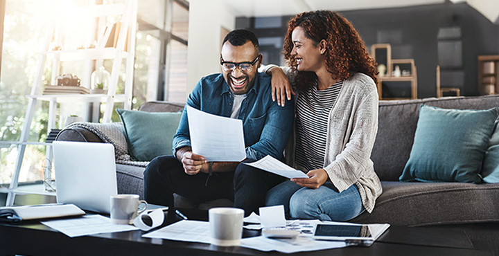 A happy couple sitting on a couch reviewing retirement documents and planning their future together
