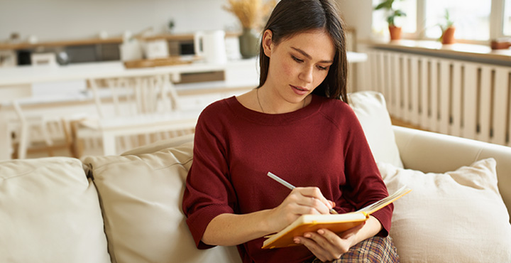 A new homeowner is on their couch writing down a list of items that they need for their new home. 