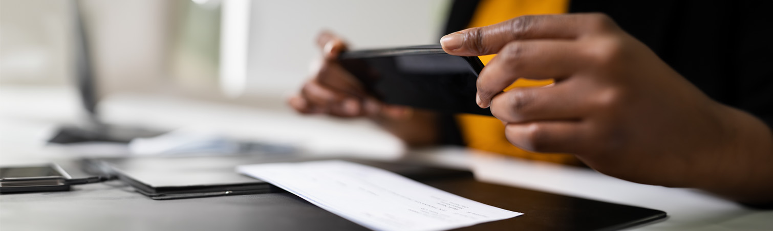 A member is taking a photo of a check on their desk with their mobile phone.
