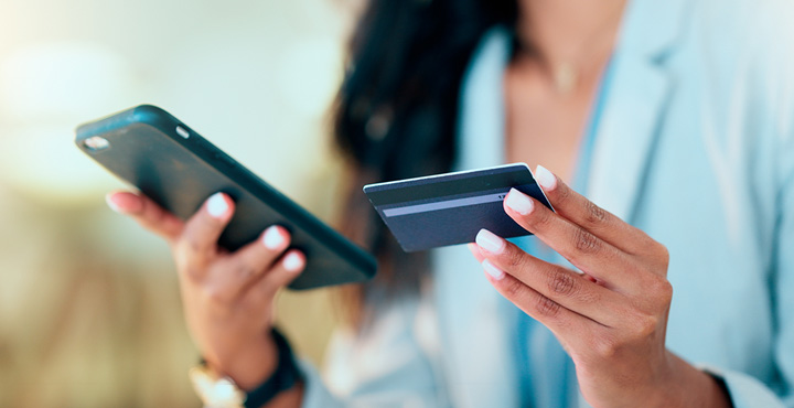 A member is looking at their phone with their card in their hand while learning how to avoid money scams. 